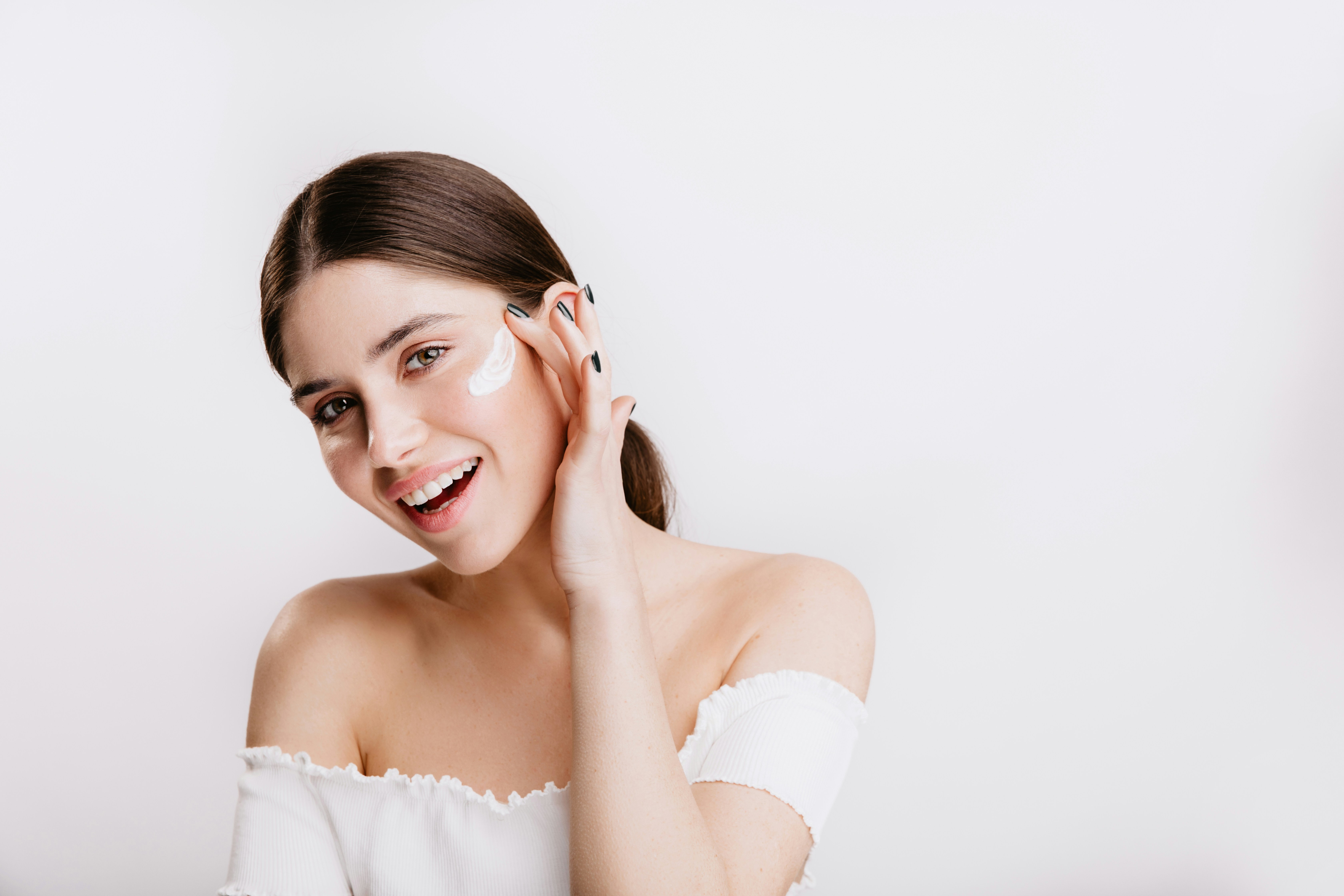 A smiling girl applying sunscreen (or moisturiser) to her face